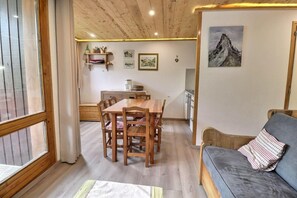 A cozy room with a wooden dining table, chairs, a sofa, and a kitchen area.