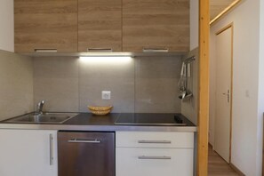 A compact kitchen with a stainless steel sink, a built-in oven, and a microwave. There is a wooden cabinet above the countertop and a door to the right.