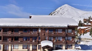 Et hotel med flere etager og altaner, med et snedækket bjerg i baggrunden og en skibakke.