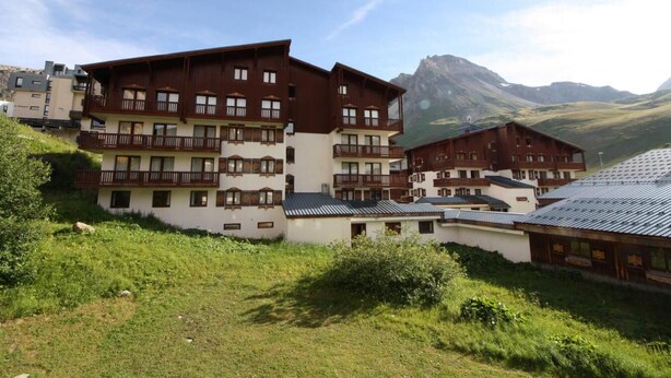 A multi-story hotel with balconies, set against a mountainous backdrop.