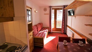 A compact kitchen with a stove, a small dining table with a red tablecloth, and a sofa with red and white bedding.