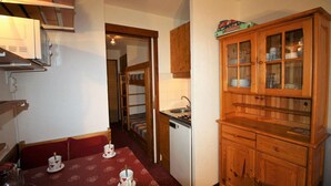 A compact kitchen with wooden cabinets, a dining table with heart-patterned tablecloths, and a bunk bed in the adjacent room.