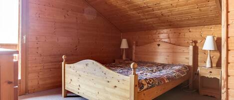 A wooden cabin bedroom with a single bed, two bedside tables, and a window.