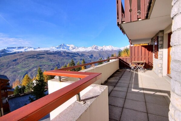 A balcony with a view of snow-capped mountains, a stone wall, and a wooden railing.