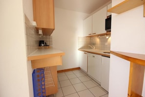 A compact kitchen with white cabinets, a wooden countertop, and a tiled floor.