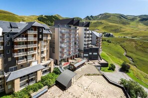 A multi-story hotel with balconies, a terrace, and a view of green hills.