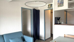 A compact living space with a sofa, a dining table, a coffee machine, and a painting on the wall.