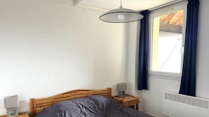 A bedroom with a wooden bed, a nightstand with a lamp, a window with curtains, and a radiator. - Floor -1, jacuzzi, hammam, terrace, balcony, tv, ski locker, 28m², Peyragudes (Germ)