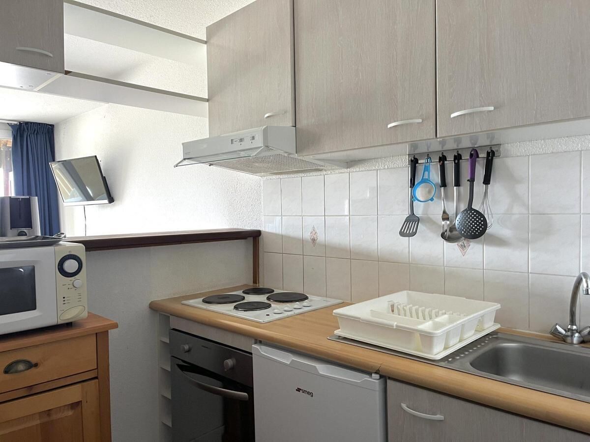 A compact kitchen with a microwave, stove, sink, and hanging utensils.