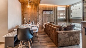Ein modernes Interieur mit Holzboden, einer Essecke mit Tisch und Stühlen, einer Couch und einem großen Fenster mit Blick auf eine verschneite Landschaft.