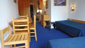 Een kamer met twee éénpersoonsbedden, een houten bureau met stoel, een klein tafeltje met lamp en een kledingkast.