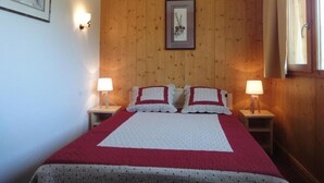Ein Schlafzimmer mit einer holzverkleideten Wand, einem gerahmten Bild, zwei Nachttischlampen und einem Bett mit einer rot-weißen Steude.