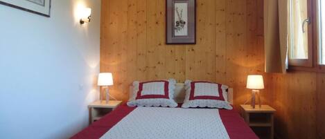 A bedroom with a wooden paneled wall, a framed picture, two bedside lamps, and a bed with a red and white quilt.