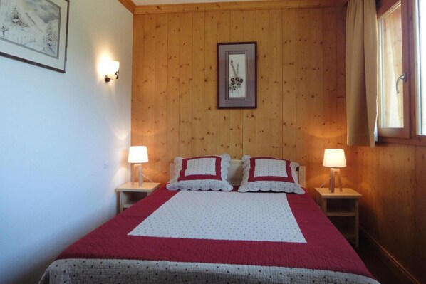A bedroom with a wooden paneled wall, a framed picture, two bedside lamps, and a bed with a red and white quilt.