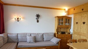 Ein gemütliches Wohnzimmer mit einem gemusterten Sofa, Holzschränken und einem Esstisch.