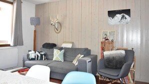 A cozy living room with a grey sofa, a blue armchair, and a wooden wall with a deer head decoration.