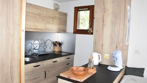 A compact kitchen with wooden cabinets, a black countertop, a sink, a coffee maker, and a small window.