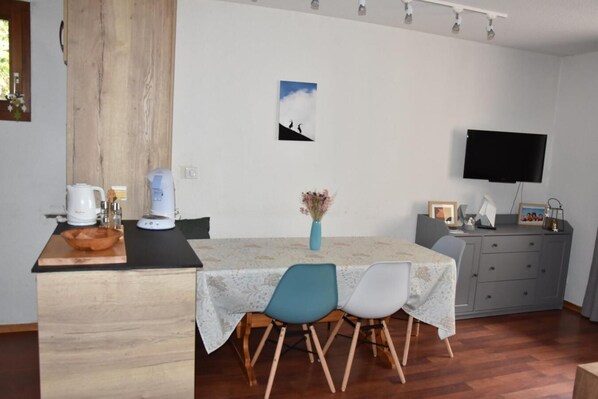 A compact kitchen with a dining area, wooden cabinets, a coffee maker, and a flat-screen TV.