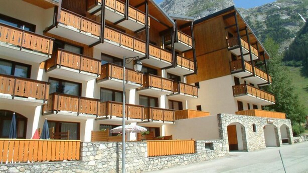 A multi-story hotel with wooden balconies, stone facade, and mountain views.