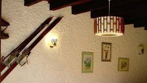 Une pièce chaleureuse avec un plafond en bois, un canapé agrémenté de coussins rouges et une table recouverte d’une nappe à motifs floraux.