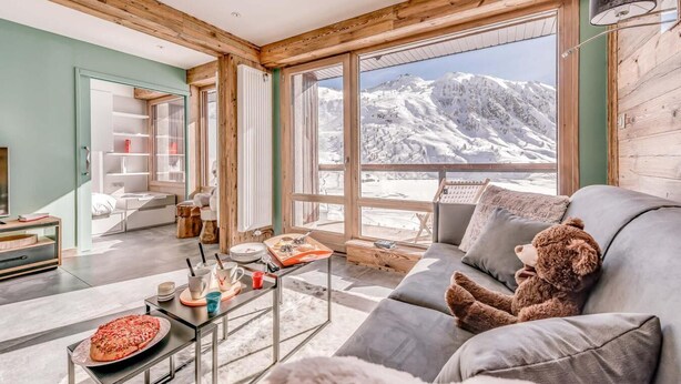Un salon moderne doté d’une grande fenêtre donnant sur un paysage montagneux enneigé.