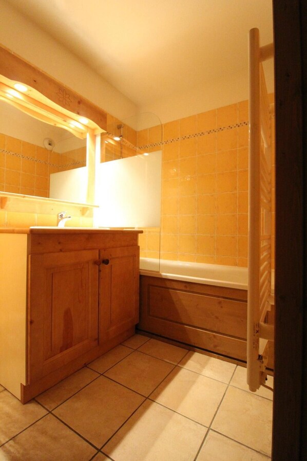 A bathroom with wooden cabinets, a sink, a mirror, and a bathtub.