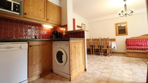 A compact kitchen with wooden cabinets, a washing machine, and a dining area with a wooden table and chairs.