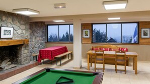A pool table with a green felt surface, a wooden bench, a red table with a patterned tablecloth, and a wooden dining table with chairs.
