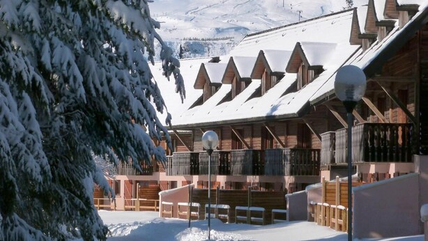 A snow-covered lodge with wooden cabins and a mountain backdrop.
