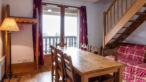 A dining area with a wooden table and chairs, a lamp, and a view through a window with purple curtains.