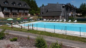 A swimming pool with lounge chairs and umbrellas, surrounded by buildings with balconies and a clear sky.