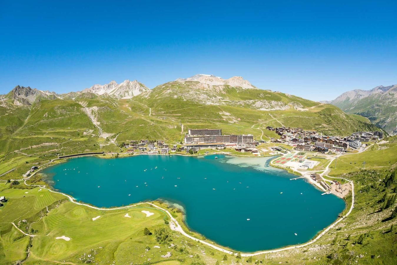 A lakeside resort with a central building surrounded by mountains, a marina, and a golf course.