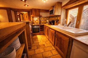 Una cocina rústica con armarios de madera, salpicadero de azulejos y suelo de piedra.