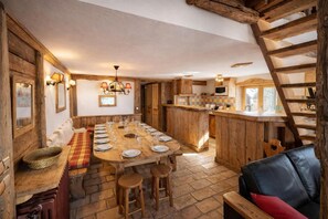 Eine rustikale Küche mit einem großen Holztisch, gedeckt für eine Mahlzeit, Holzbalken an der Decke und Steinböden.
