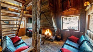 L’intérieur d’un chalet rustique, avec une cheminée en pierre, des murs en bois et des canapés en cuir agrémentés de coussins rouges.
