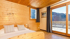 Dormitorio con paneles de madera, una cama grande, dos ventanas y vistas a un paisaje nevado.