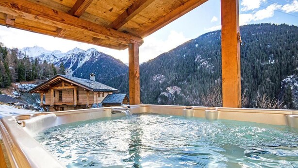Una cabaña de madera con jacuzzi y vistas a un paisaje montañoso.