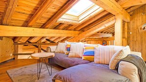 Acogedor dormitorio en ático con vigas de madera, un conjunto de sofás y una pequeña mesa redonda.