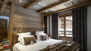 Une chambre confortable avec un plafond en bois, un grand lit avec une literie blanche et marron, un plaid en fausse fourrure et une fenêtre avec des rideaux.
