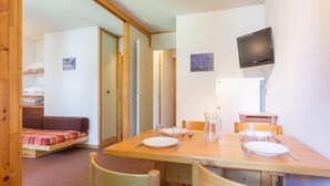 Une pièce de taille modeste comprenant une table à manger pour deux personnes, un canapé et un téléviseur fixé au mur.
