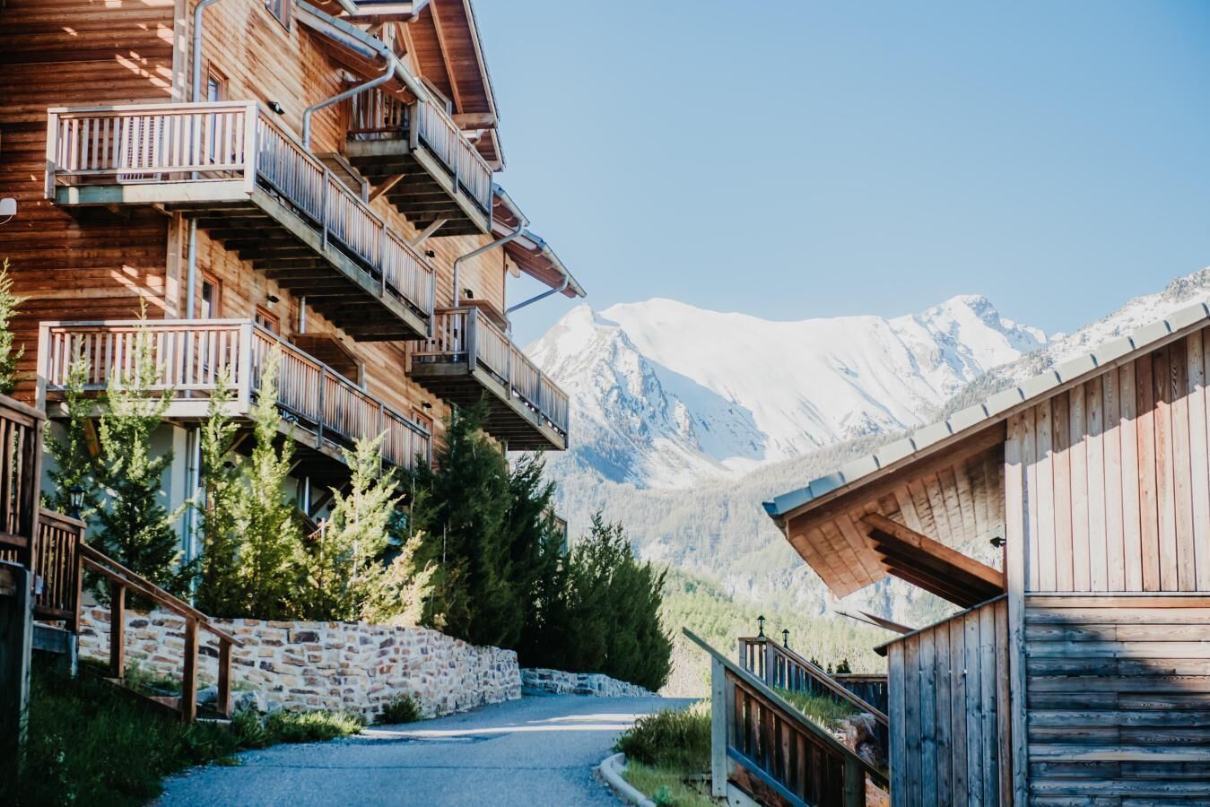 A wooden building with balconies, a stone wall, and a mountain view.