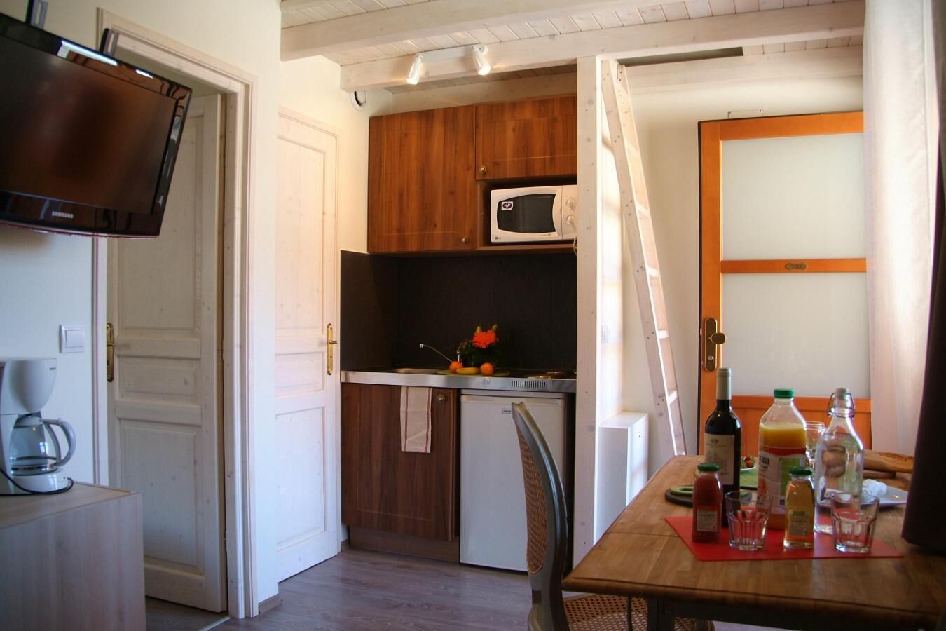 A compact kitchen with a microwave, a coffee maker, and a dining table with various bottles and glasses.