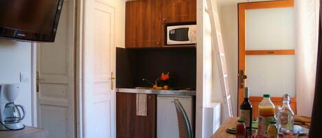 A compact kitchen with a microwave, a coffee maker, and a dining table with various bottles and glasses.