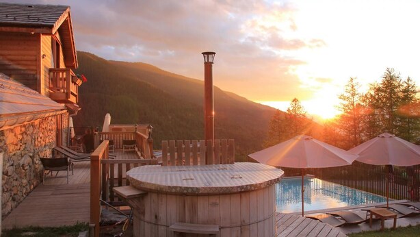 Uma cabana de madeira com hidromassagem, piscina e um terraço.