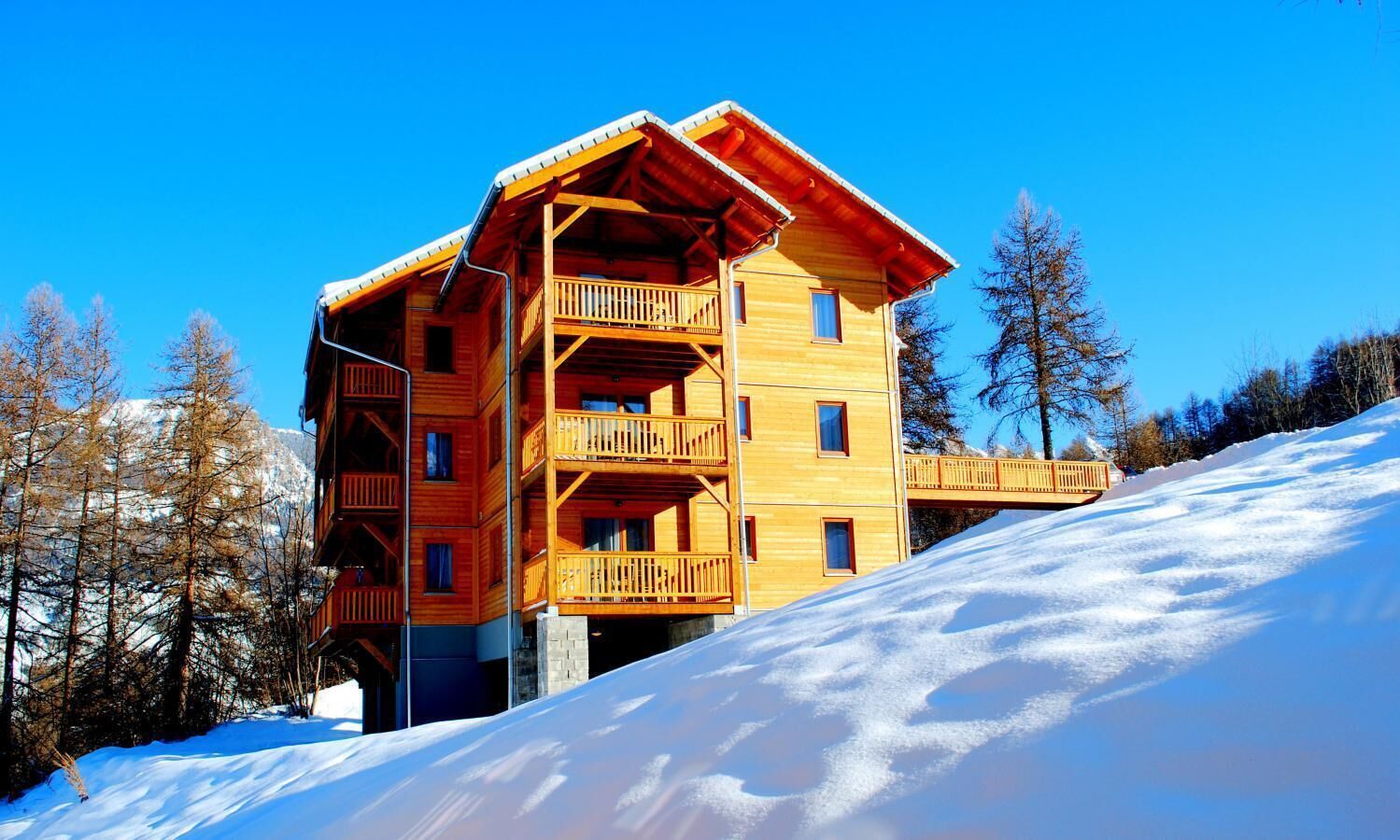 Ein mehrstöckiges Holzchalet mit Balkonen vor einer verschneiten Bergkulisse.