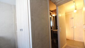 Un couloir avec une porte donnant sur une salle de bain, un luminaire et une prise électrique visible.