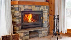 A stone fireplace with a fire burning inside, a wooden mantel, and a metal fireguard to the right.