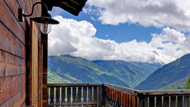 A wooden balcony with a metal railing overlooking a mountainous landscape.