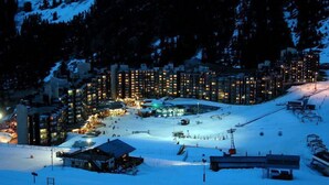 Ein schneebedecktes Skigebiet bei Nacht mit beleuchteten Gebäuden und einer Seilbahn.