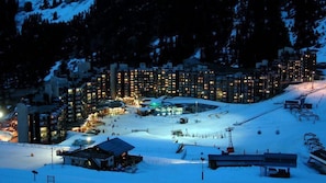 A snow-covered ski resort at night with illuminated buildings and a ski lift. - Ski-in/ski-out & foot of the slopes, 5th floor, swimming pool, balcony, tv, ski locker, 28m² (La Plagne)